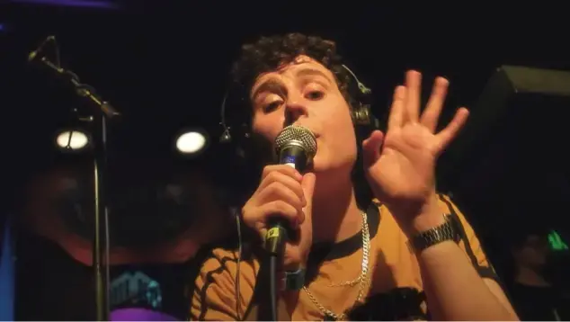 Person on stage, wearing headphones, holding microphones.