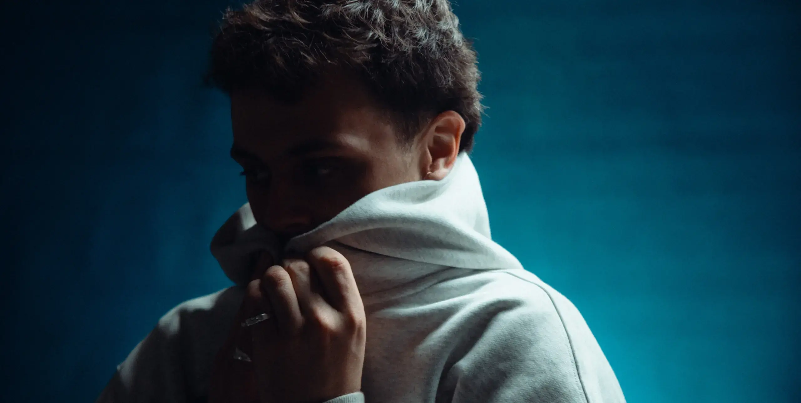 Man with short hair pulling a hoodie up around his chin.