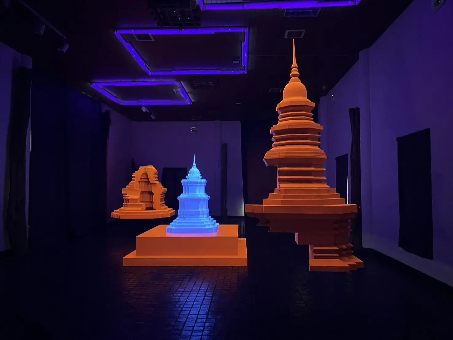 A hologram of temples is lit up in fluorescent orange and blue as an AR addition to a dark gallery space