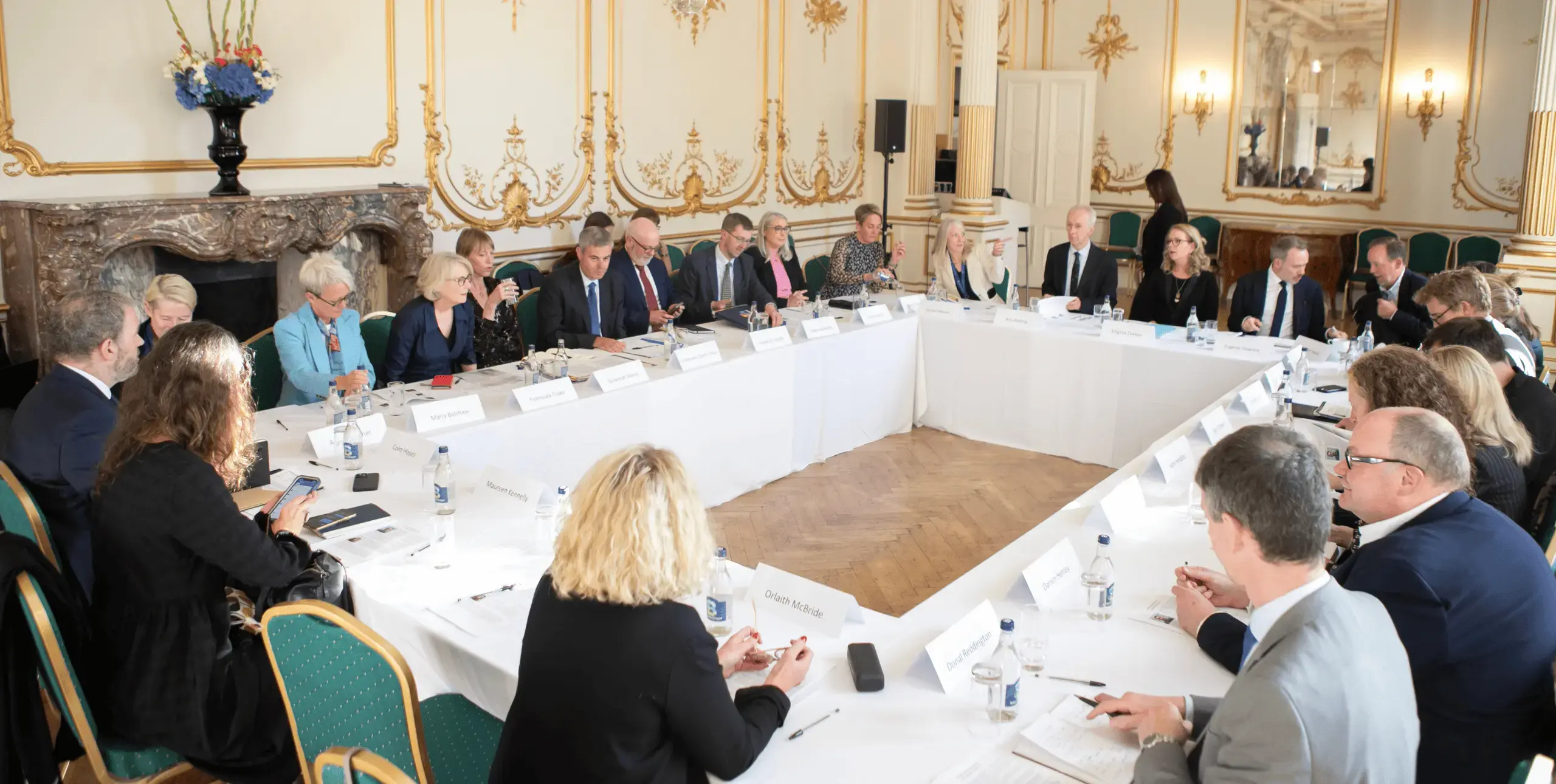 Large, formal room with many people sat around the table.