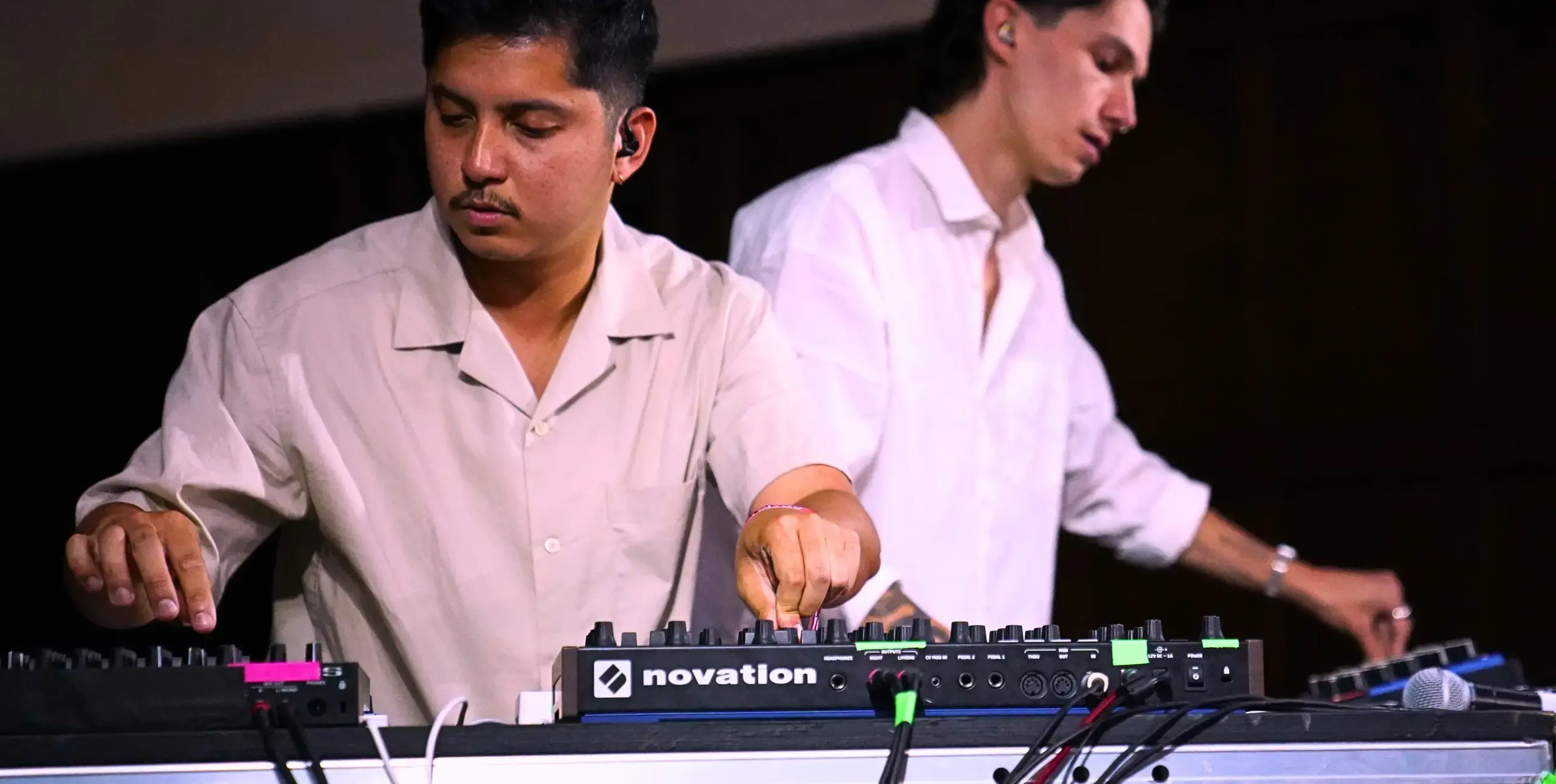 Two men on stage behind mixing desks wearing white shirts.