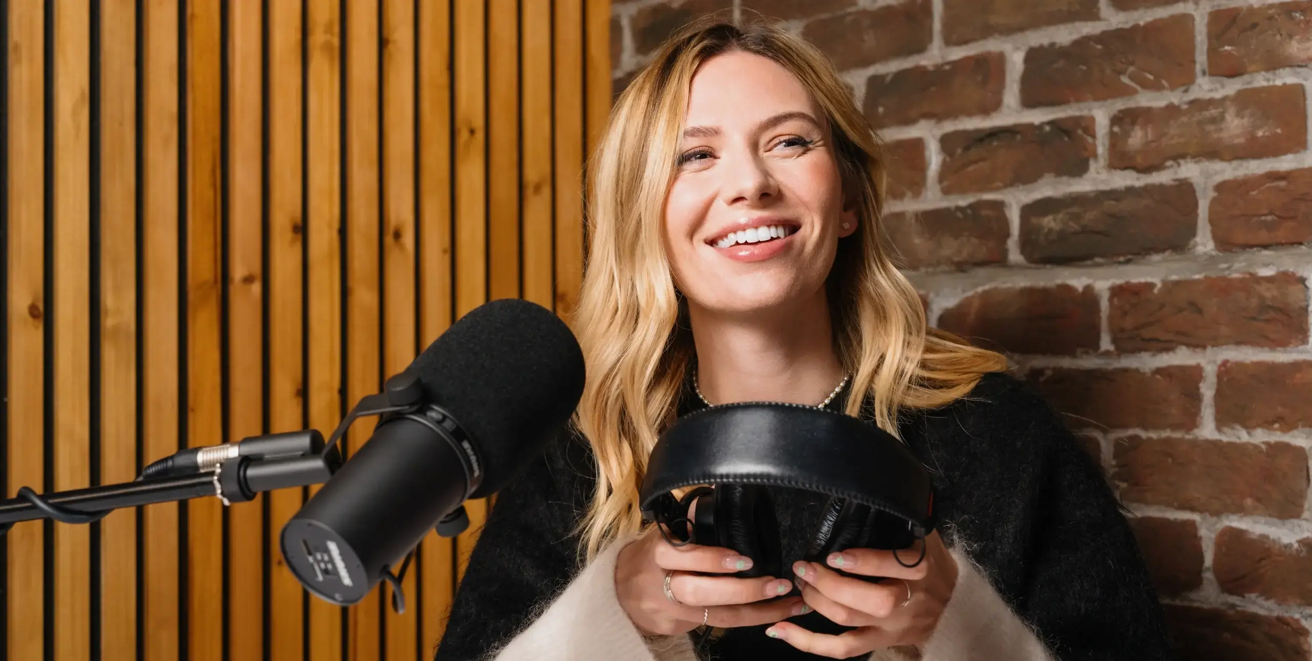 Lady sat in radio studio holding headphones, microphone in front of her.