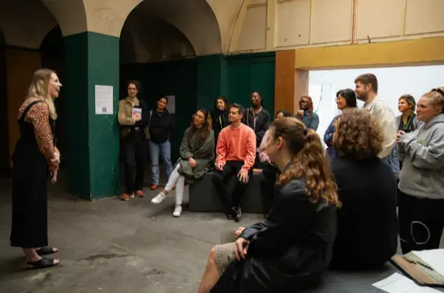 Crowd of people facing a lady stood facing them in a workshop.