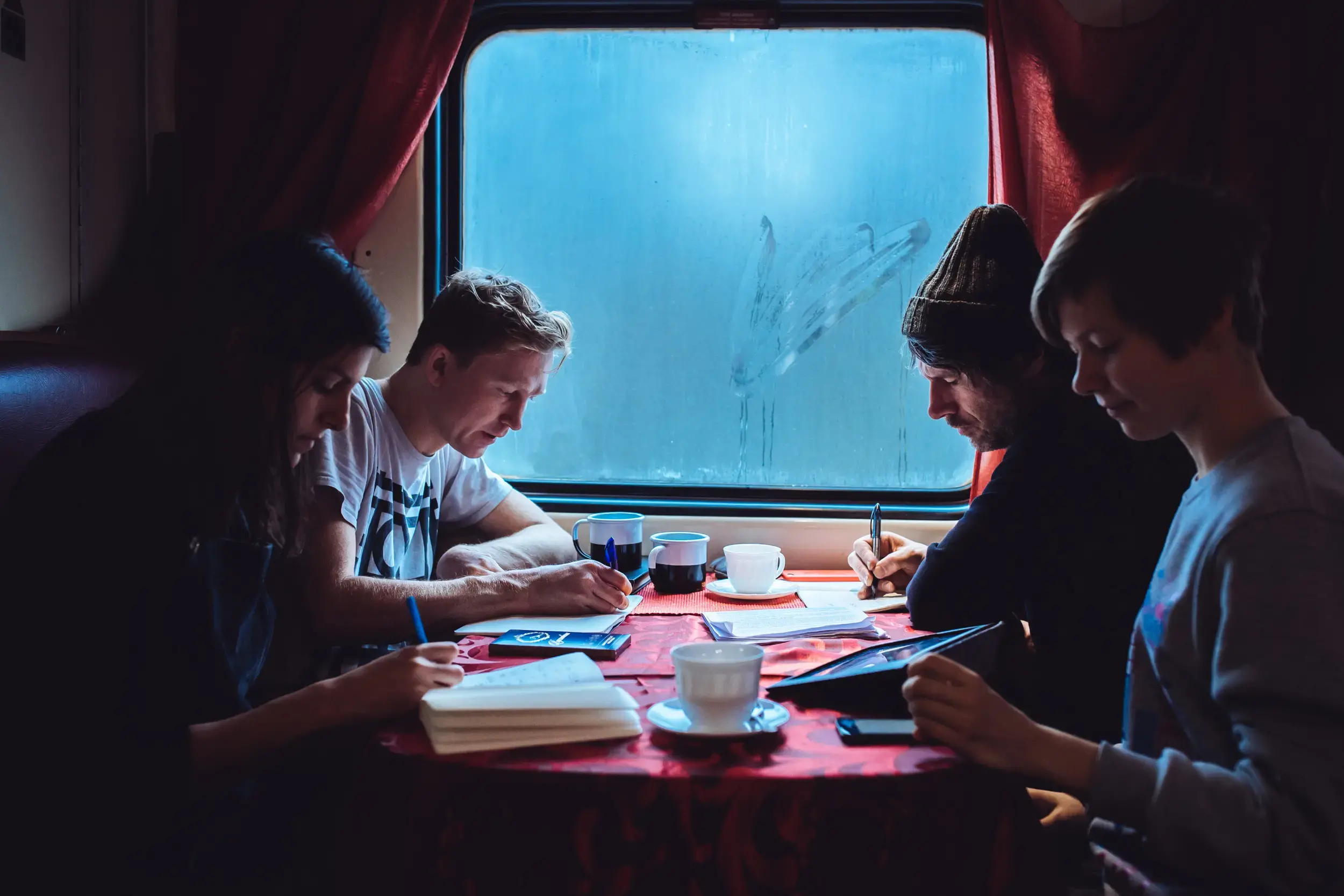 Four poets travel together on a train they are reading and writing on a train carriage against a steamy window