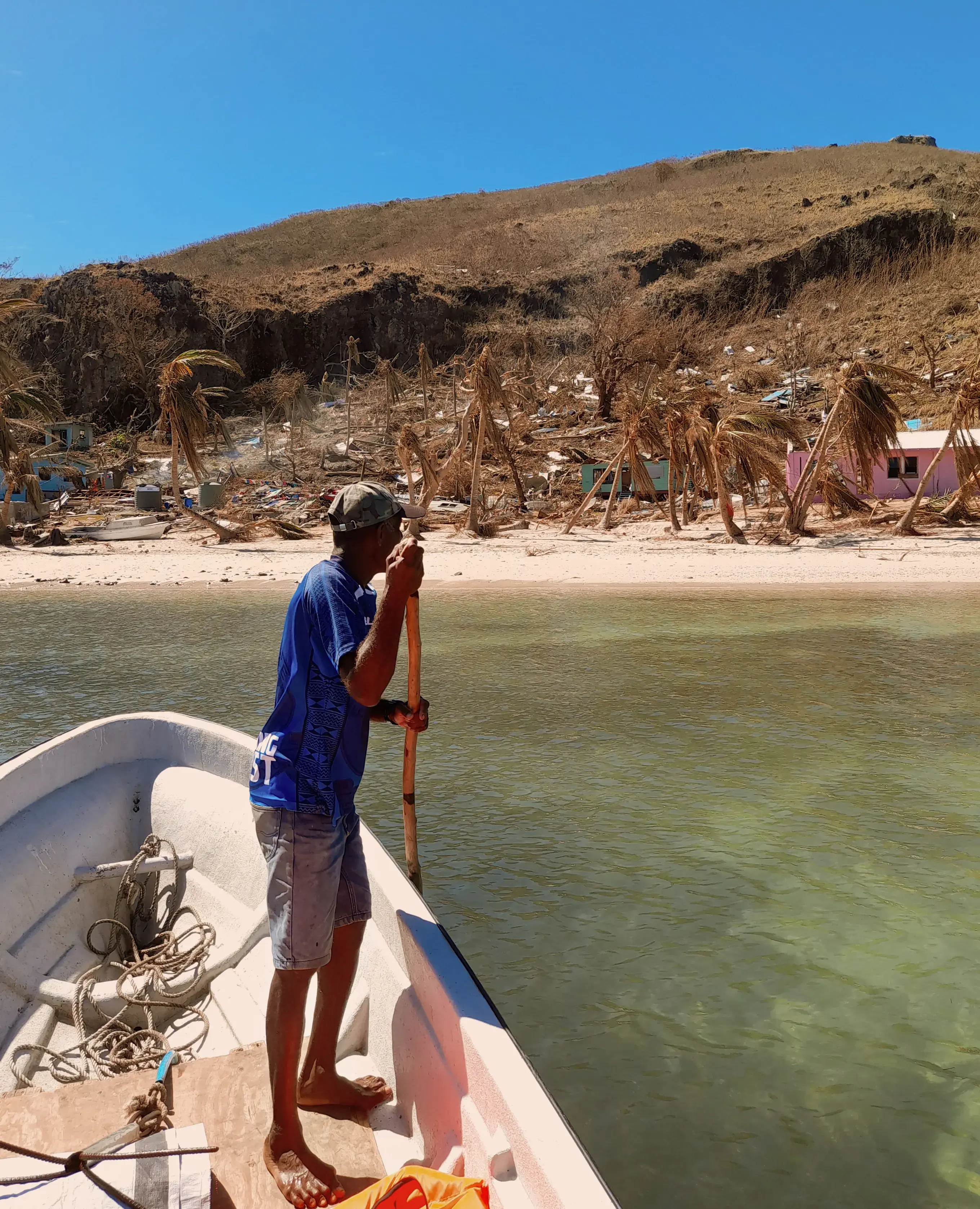 A man stands in a small wooden boat looking at his home, devastated by a tropical cyclone