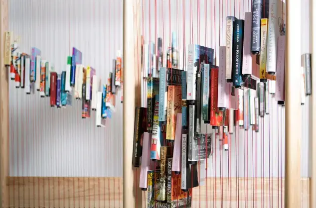 Paperback books suspended on vertical red strings at different heights, creating a zig-zag pattern.