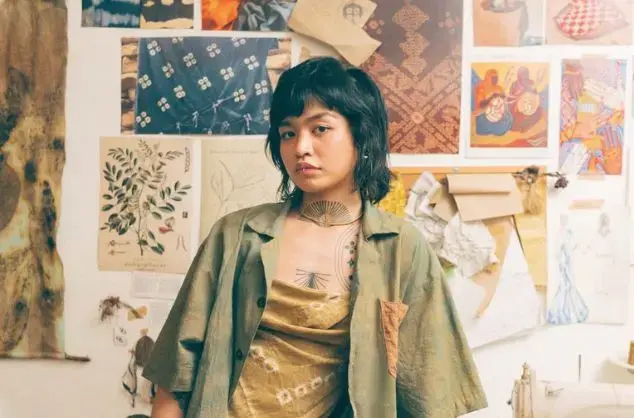 A woman stands in front of a wall with multiple images of textiles mounted to it.