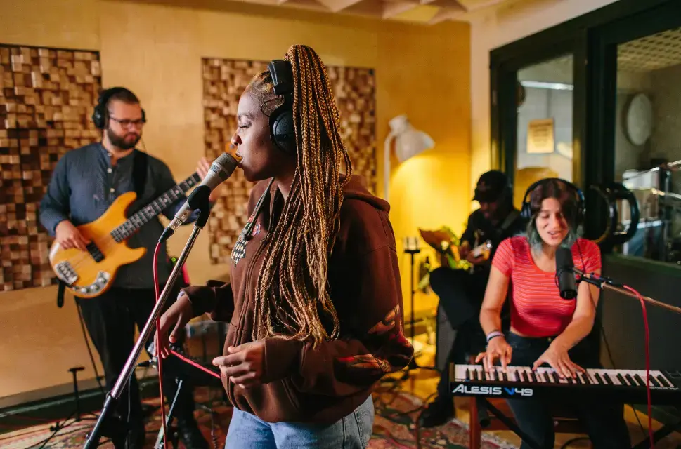 In a recording studio with a singer singing into a microphone, a bass player on the left and keyboard player sat down to the right.
