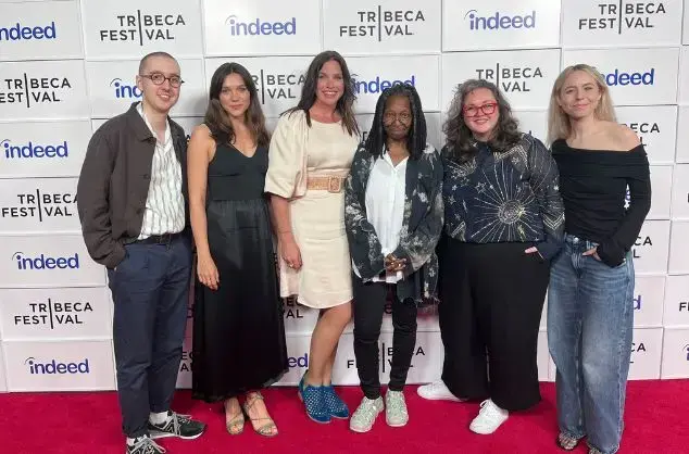 A group of six people standing together on a red carpet in front of a Tribeca Film Festival press board. 