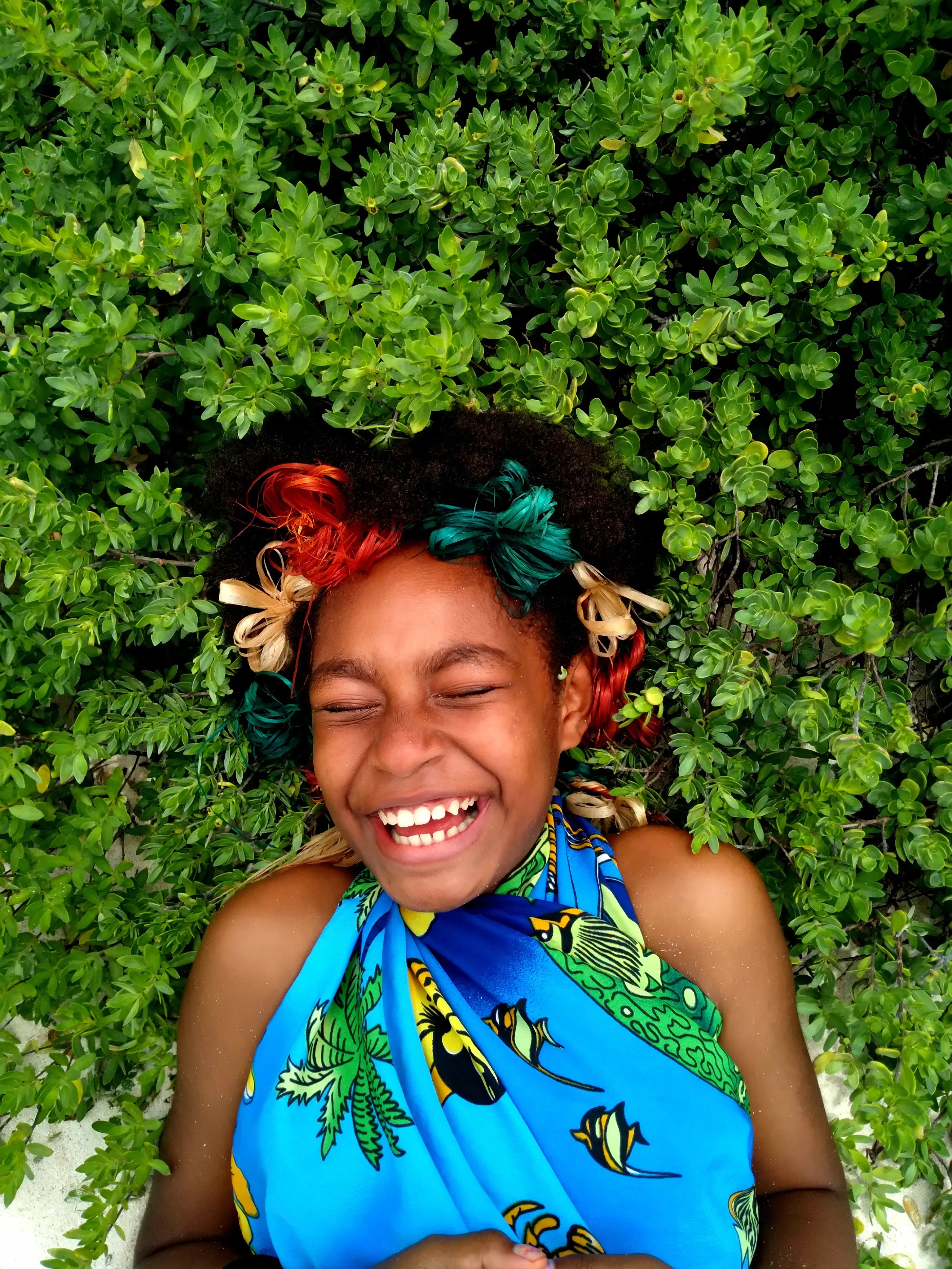 A young woman laughs as she leans back on a bed of green plants