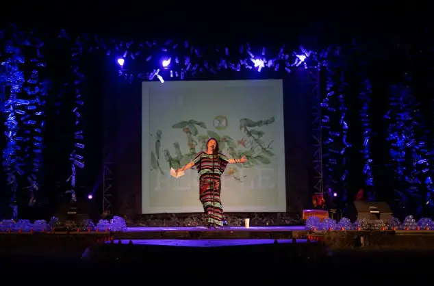 Literary activist Rufus Mufasa stands on a stage infront of a projection saying People as she performs a spoken word piece in Indonesia