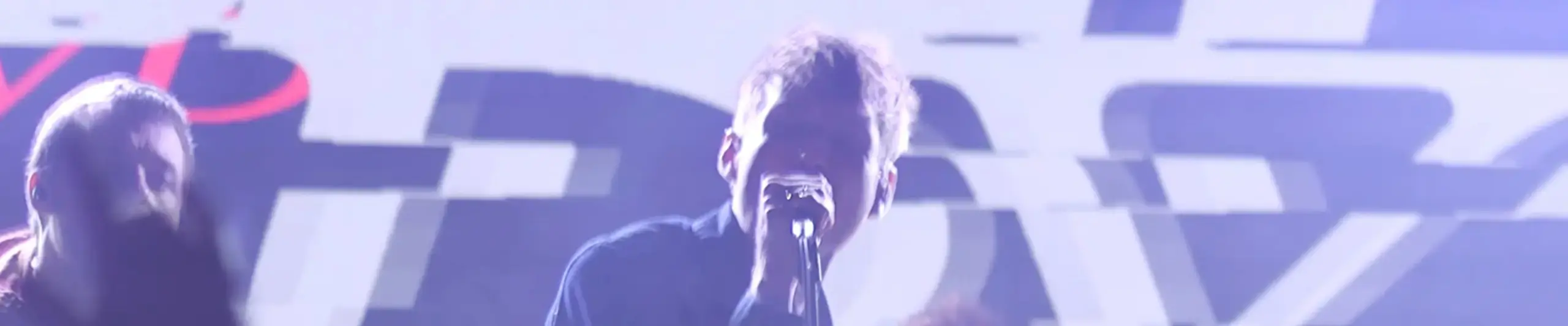 Close up on stage showing two men singing, one holding his microphone close to his mouth.