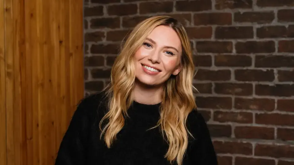 Lady with long blonde hair smiling; brick wall behind her. 