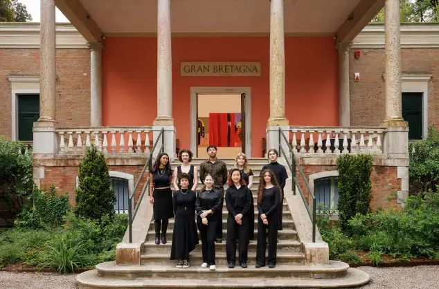 Group of nine people dressed in black standing on steps outside a building labeled Gran Bretagna.