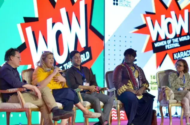 A panel of speakers sits on a stage against a backdrop showing the logo for WOW - Women of the World Festivals