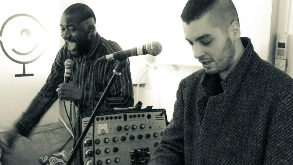 Two men performing with microphones and audio equipment indoors.