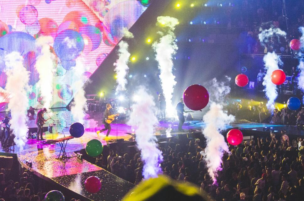 Live music event with guitarist on stage, balloons off stage and a crowd standing and seated.