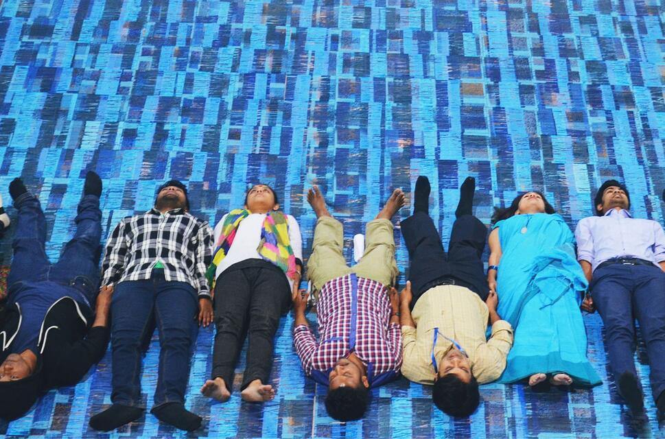Young people lying on their backs in a row all next to each other, looking upwards from a bright background.