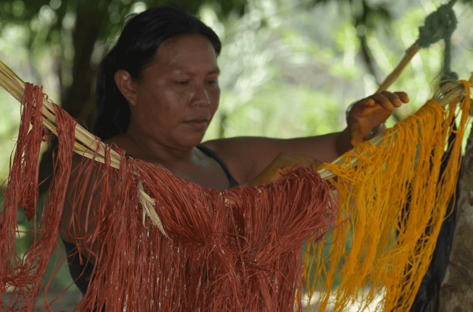 A woman works with fabric which is hanging from a tree suspended on a string.