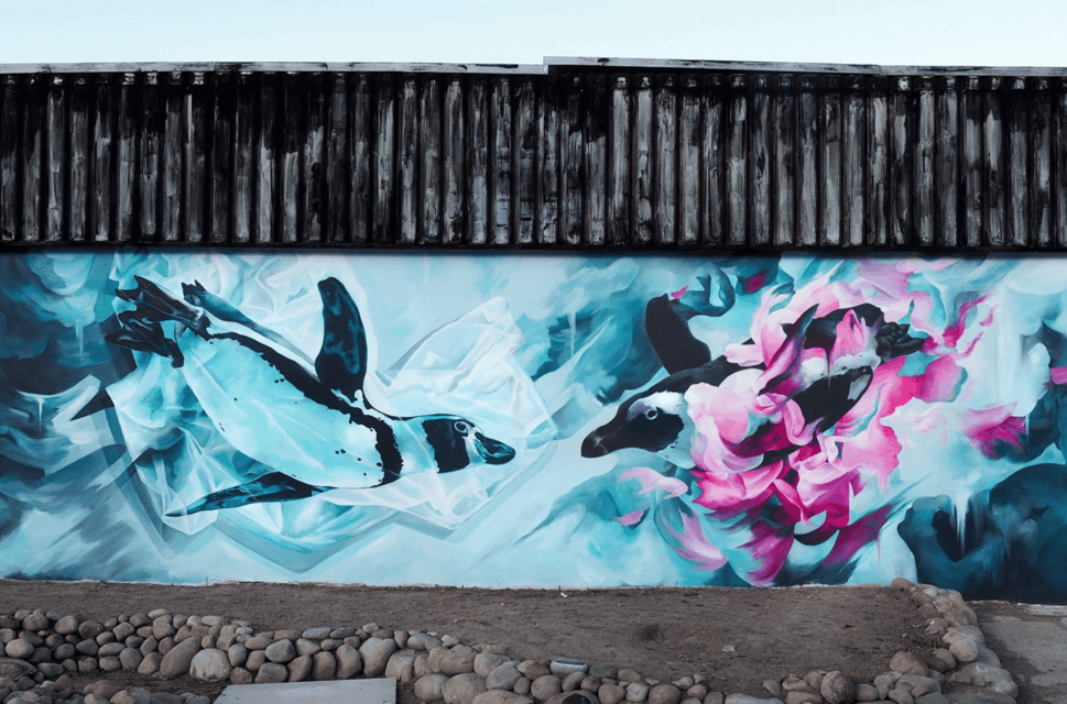 A mural of two penguins swimming underwater on a the wall of a small building with a wooden roof.