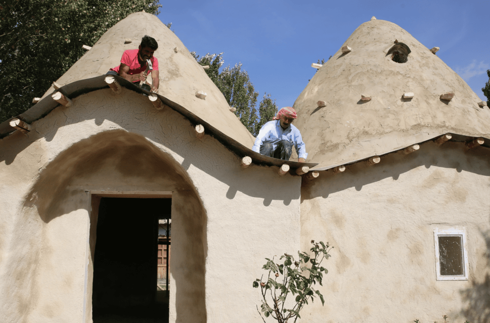 Syrian Dome Houses project. Two men work on the rooftop of a domed building in the sunshine.