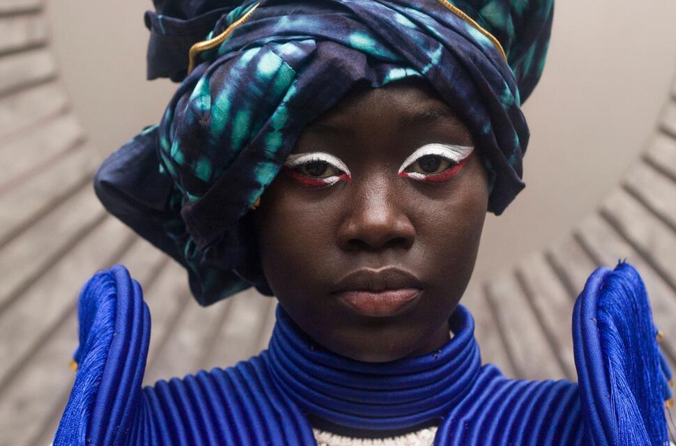 A woman models a tie-die turban and jacket with high epaulettes