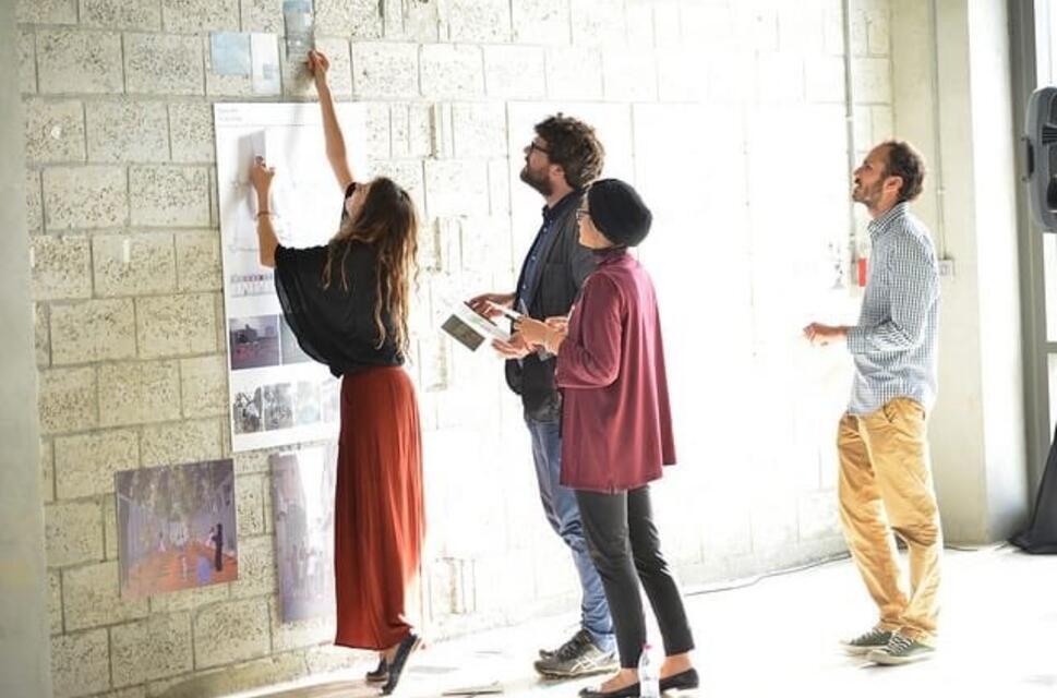 Four people pin papers to a brick wall.