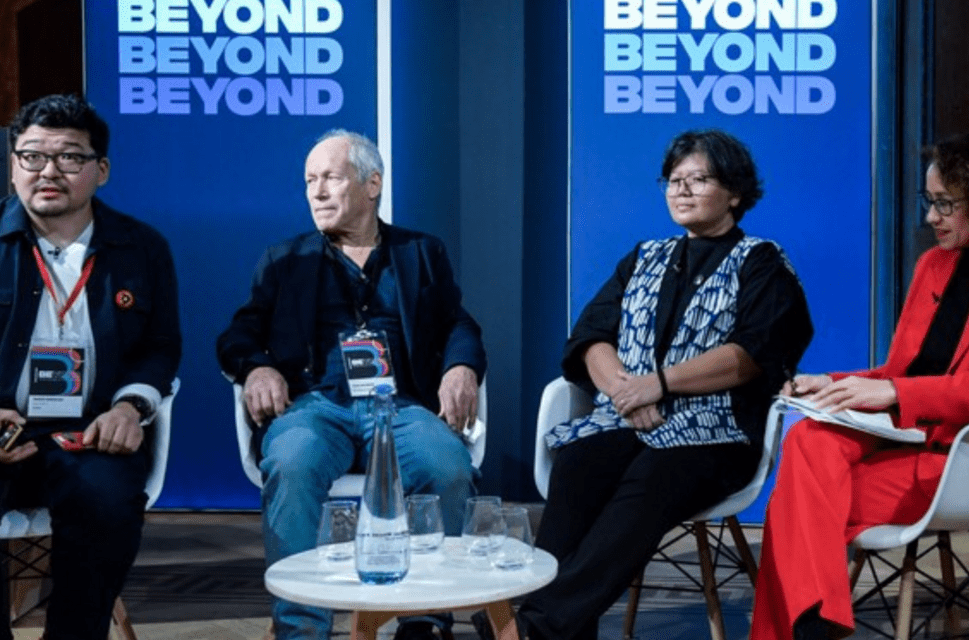 Four people seated on a stage in front of banners reading 'BEYOND' at the BEYOND conference 2023. The people are Daniar Amanaliev, John Newbigin, Tita Larasati and Samira Ahmed.