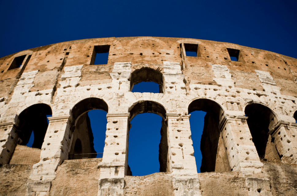 The Colosseum in Rome, photographed from beneath, with bright blue sky showing above and in betweem the columns.