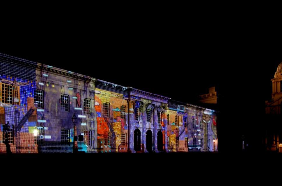 A row of historic looking brick buildings are lit up with colourful projections at night