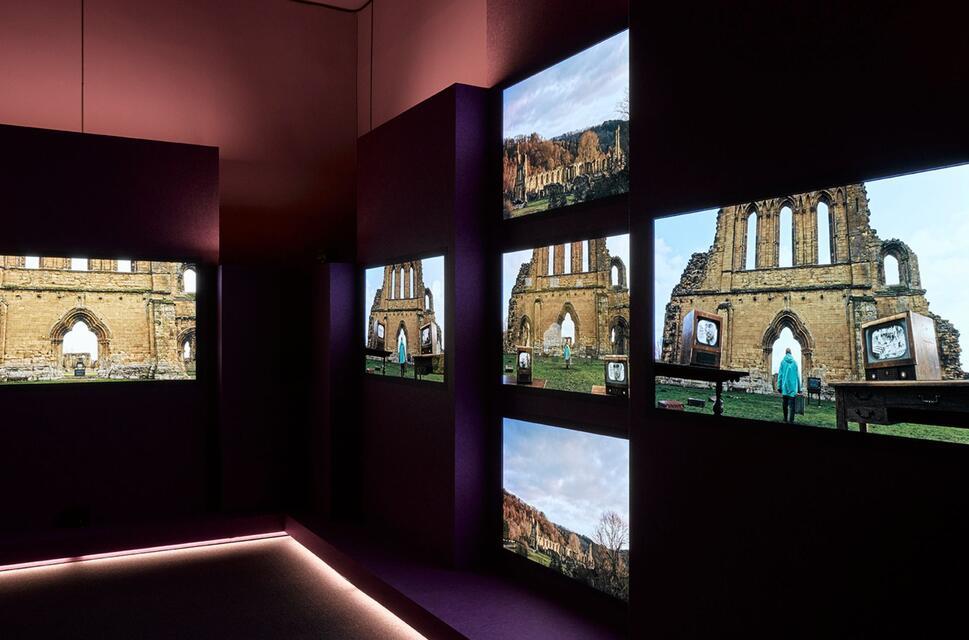 A still from John Akomfrah's Listening All Night To The Rain featuring 6 screens all showing different views of a ruined church.
