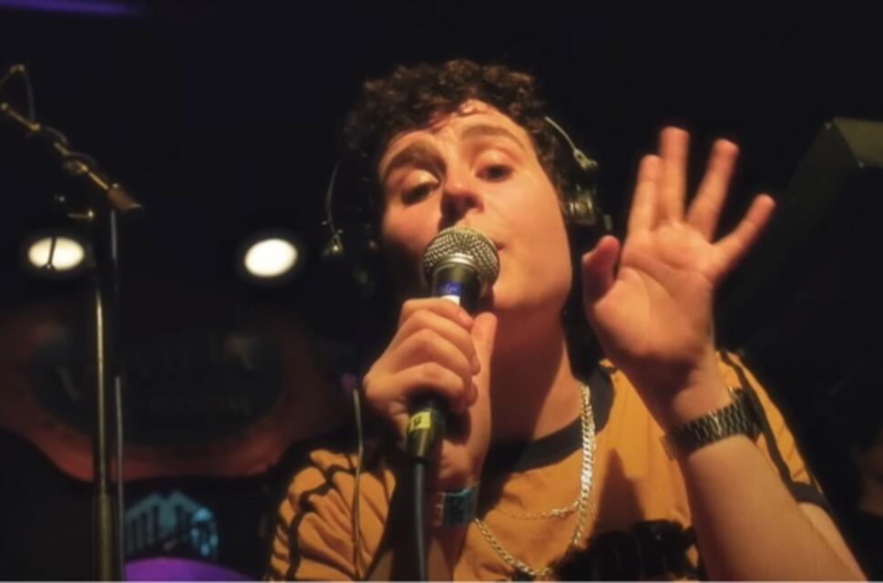 Person on stage, wearing headphones, holding microphones.