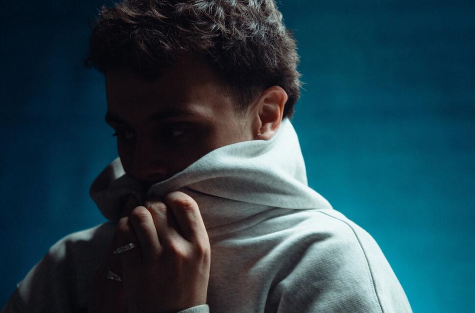 Man with short hair pulling a hoodie up around his chin.