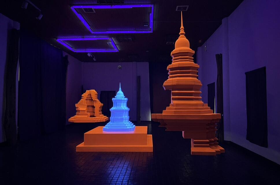 A hologram of temples is lit up in fluorescent orange and blue as an AR addition to a dark gallery space