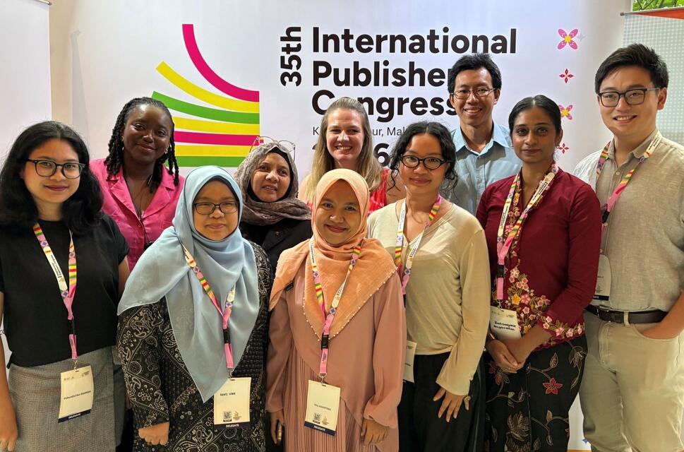A diverse group of 10 people smiling at the camera in front of a conference backdrop