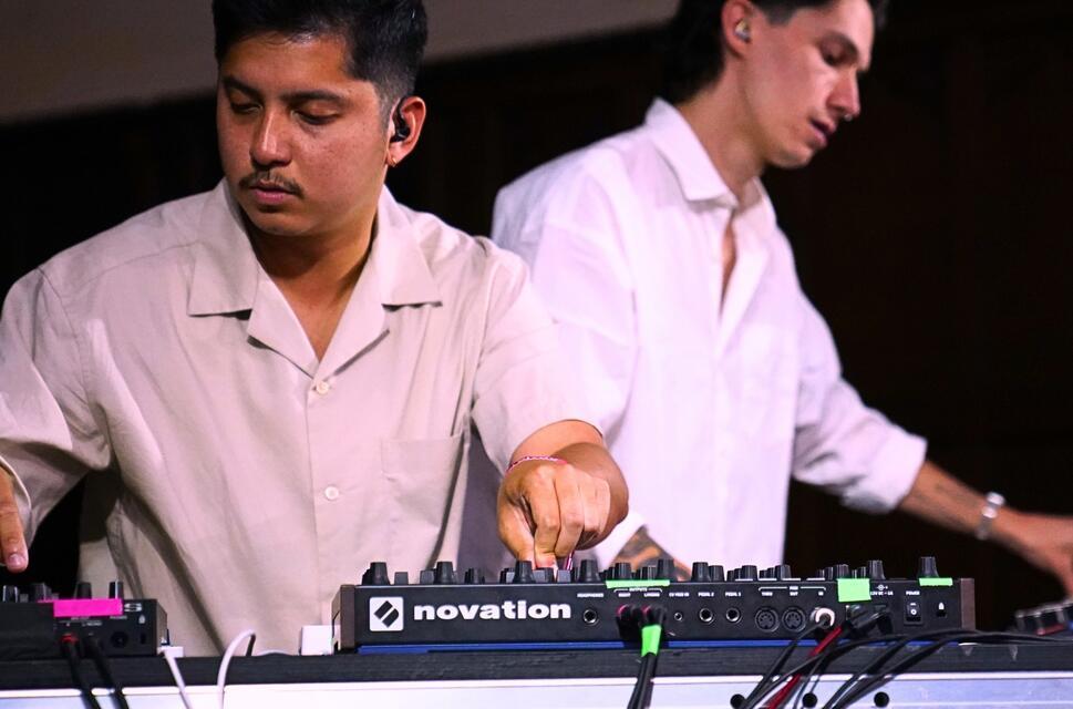 Two men on stage behind mixing desks wearing white shirts.