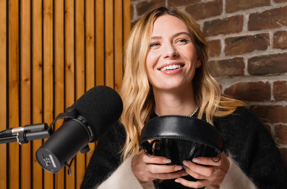 Lady sat in radio studio holding headphones, microphone in front of her.
