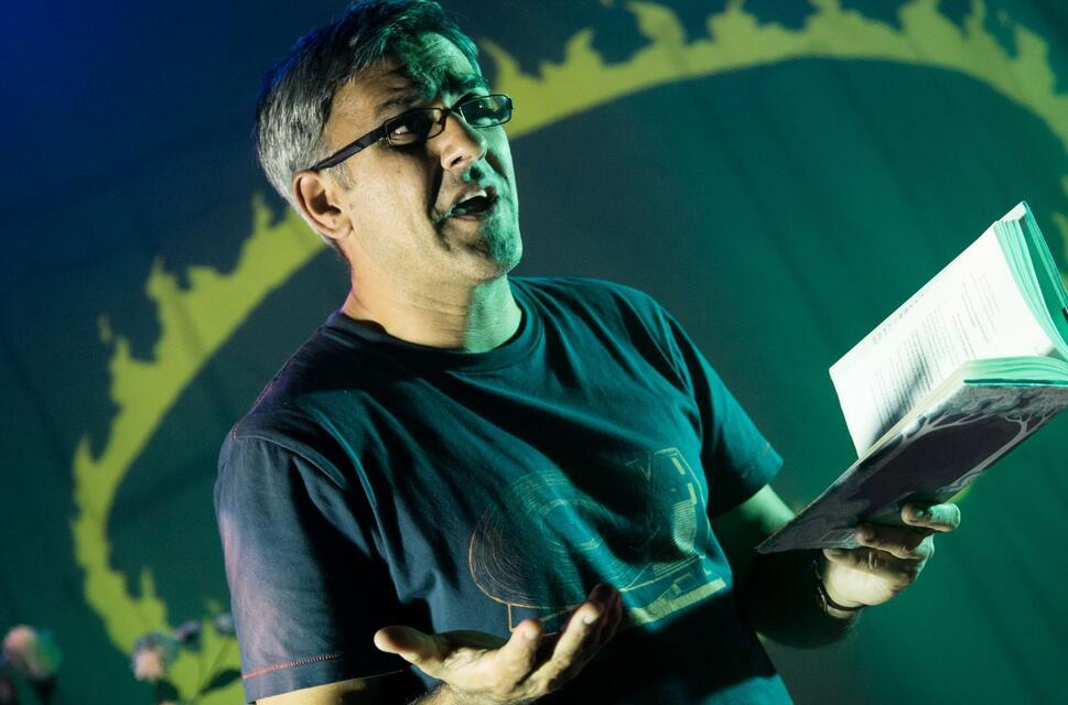 British Poet Daljit Nagra stands on stage and animatedly reads from an open book