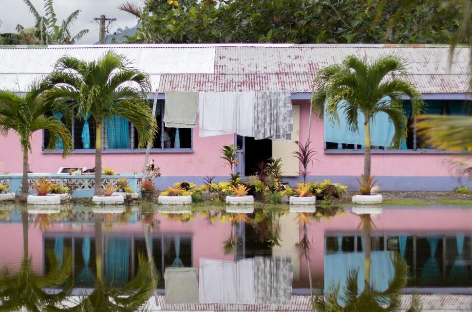 A pink bungalow is reflected in the huge puddle of water in front of it
